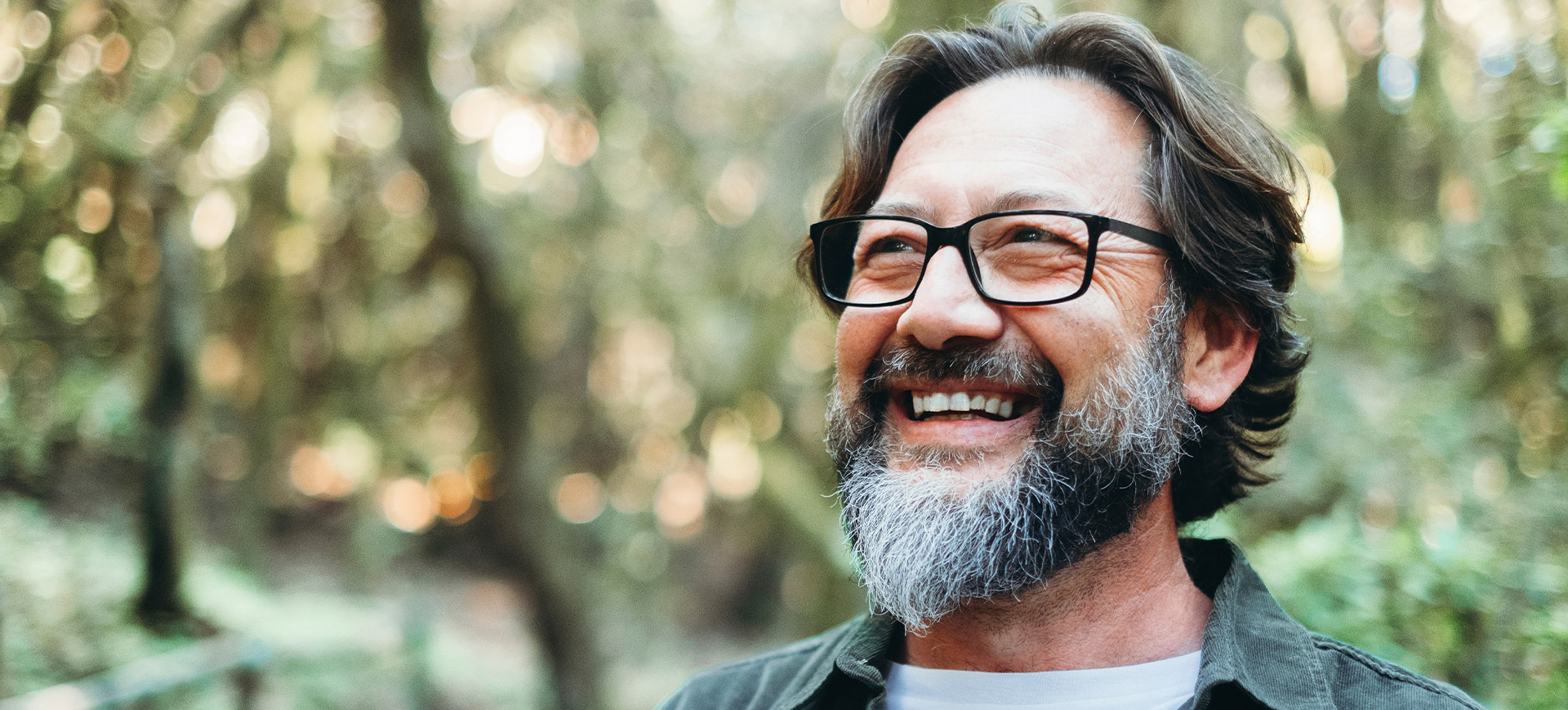 A man with thick-rimmed glasses smiling outdoors