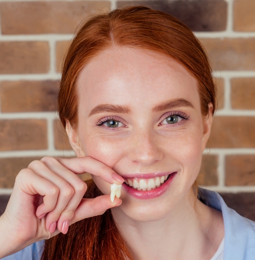 Smiling woman holding a tooth after tooth extractions in Colorado Springs